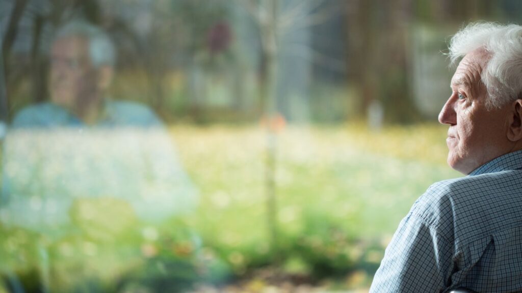 ein einsamer älterer Herr sitzt alleine am Fenster und schaut in die Ferne