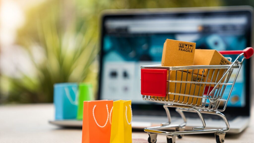 Einkaufswagen mit vielen Tüten vor einem Notebook