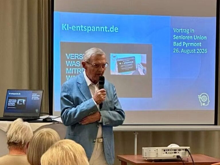Ein Mann mit Mikrofon spricht vor der Leinwand mit der Folie „KI-entspannt.de – Vortrag in Senioren Union Bad Pyrmont, 26. August 2026“, im Vordergrund das Publikum